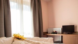 A hotel room with a bed, a desk with a TV, and a window with curtains. - Hotel Adler (Foppolo)