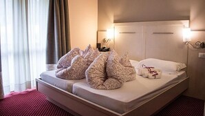 A hotel room with a bed, pillows, a nightstand, and a window with curtains. - Hotel Adler (Foppolo)