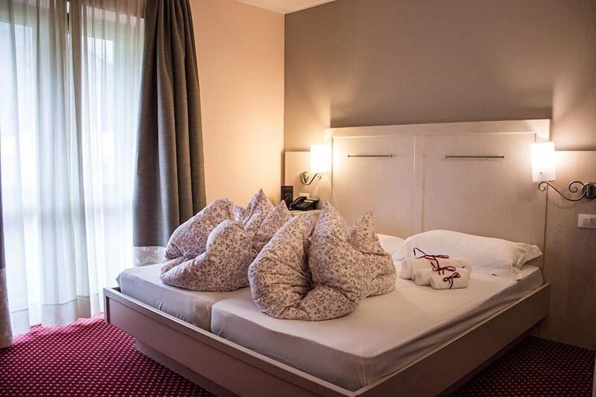 A hotel room with a bed, pillows, a nightstand, and a window with curtains.