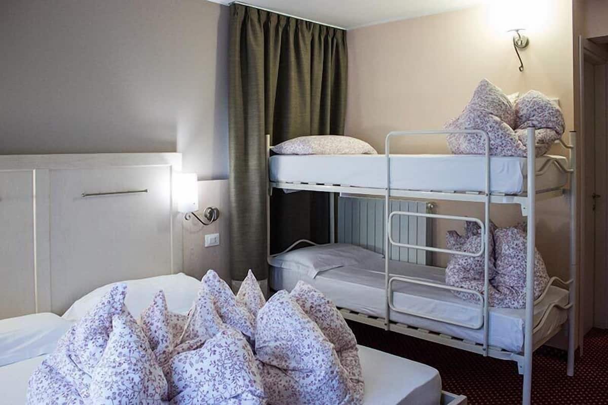 A hotel room with a bunk bed, a bedside table with a lamp, and a large window with curtains.
