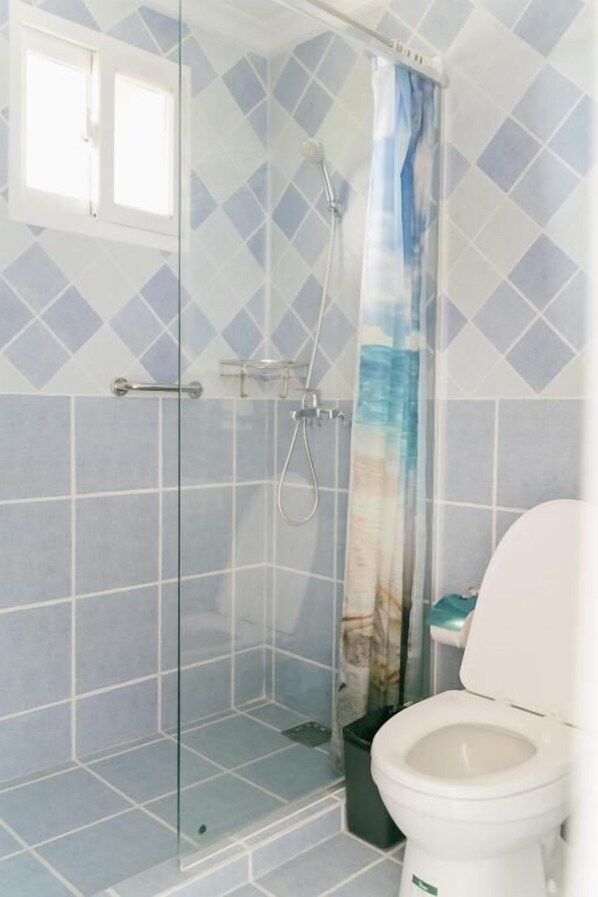 A bathroom with a glass shower enclosure, a toilet, and a window. - Saipan Emerald Villa (Saipan)