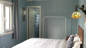 Un dormitorio con cama, ventana, puerta y aire acondicionado instalado en la pared.