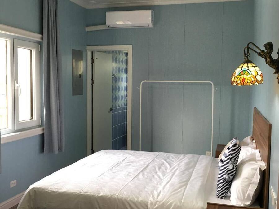 A bedroom with a bed, a window, a door, and a wall-mounted air conditioner.