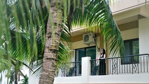 Un balcon avec un palmier, une personne et un bâtiment doté d’une fenêtre et d’un appareil de climatisation.
