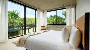 A bedroom with a large bed, a view of palm trees, and a balcony.