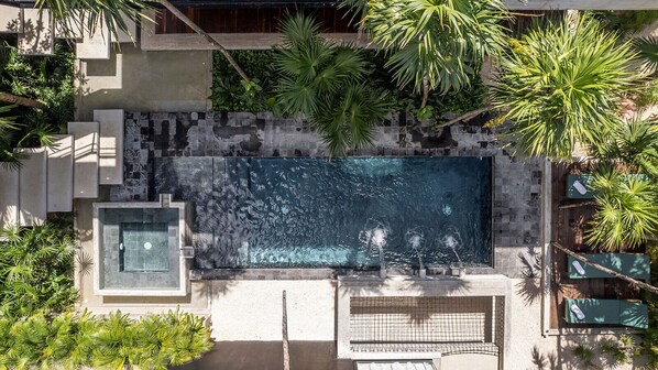An aerial view of a rectangular swimming pool surrounded by palm trees and concrete structures.