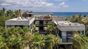 A modern multi-story building with a rooftop terrace, large windows, and a view of the ocean.