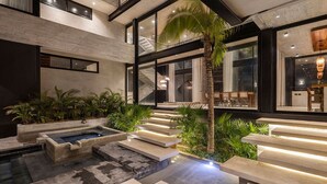 A modern indoor pool area with a staircase, palm trees, and a seating area.