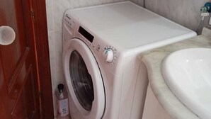 Een praktische, moderne wasruimte met een voorlader wasmachine, een kleine fles wasmiddel en een wasbak.
