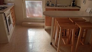 Een keuken met een fornuis, oven en een raam met gezoet glas. Er staan houten stoelen en een wastafel met kraan.