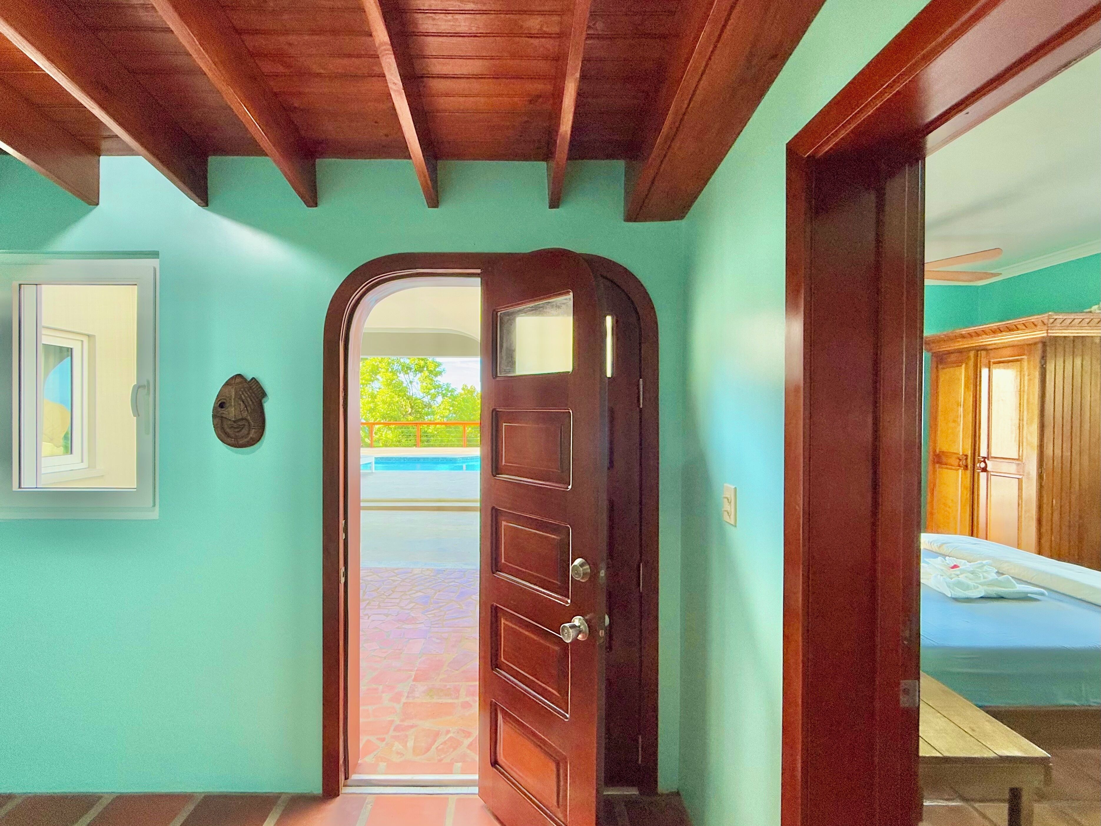 A wooden door leading to a room with a bed and a view of a swimming pool.