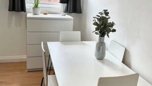 A modern dining area with a white table and chairs, a window with curtains, and a potted plant on the windowsill. - Modern, fresh & spacious apartment with parking (Bristol)