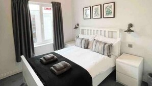 A bedroom with a bed, bedside tables, a window with curtains, and wall-mounted artwork. - Modern, fresh & spacious apartment with parking (Bristol)