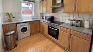 A modern kitchen with wooden cabinets, a washing machine, a microwave, a stove, and a trash bin. - Modern, fresh & spacious apartment with parking (Bristol)