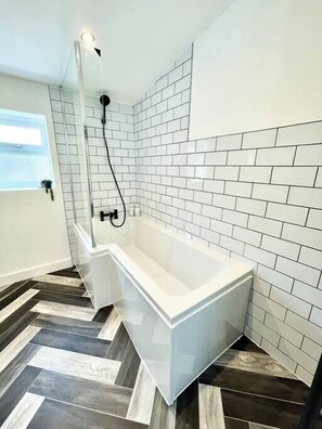 Ein modernes Badezimmer mit einer rechteckigen Badewanne, weißen Fliesenwänden und einem Fischgrätparkettboden.