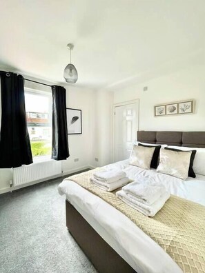 Ein Schlafzimmer mit Bett, Heizkörper, Fenster mit schwarzen Vorhängen und einem Wandbild.