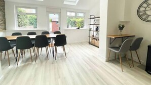 A modern dining area with a high ceiling and skylights, a wooden table with chairs, and a bookshelf. - Hereford House – Sleeps 8! BS2 (Bristol)