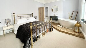 A bedroom with a large bed, a vanity, a bathtub, and a hanging light fixture. - The Penthouse BS3 (Bristol)