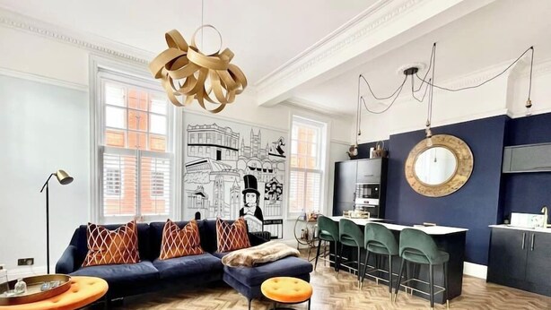 A modern living room with a sofa, ottoman, and a herringbone wood floor. - The Penthouse BS3 (Bristol)
