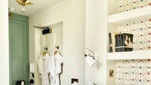 A bedroom with a bed, a wardrobe, a robe, a towel rack, and a shelf with books and a framed photo. - Pulteney Bridge Suites - Apartment 2A (Bath)