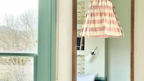 A bedroom with a bed, a hanging lamp, a mirror, and a view of a garden. - Pulteney Bridge Suites - Apartment 2A (Bath)