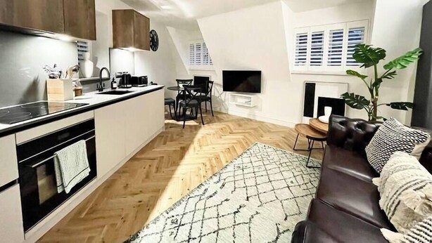 Ett modernt kök med ett fiskbensmönstrat golv, en matplats med tv och en mysig sittgrupp med en mönstrad matta.