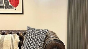 En mörkbrun lädersoffa med en mönstrad pläd och en inramad tavla som föreställer en stadsbild på väggen.