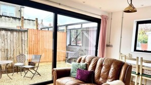 A cozy living room with a leather sofa, a dining table, and a large sliding glass door leading to an outdoor patio.