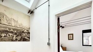 A room with a wooden herringbone floor, a bed with a green blanket, a framed picture on the wall, and a skylight above the staircase.