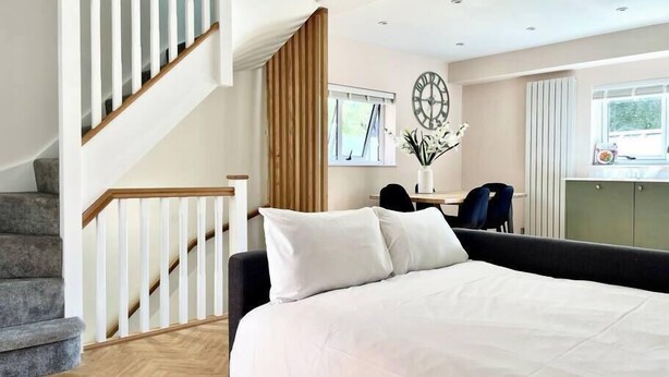 Une chambre à coucher avec un grand lit, un escalier en bois, un bureau avec des chaises et une fenêtre avec des rideaux.