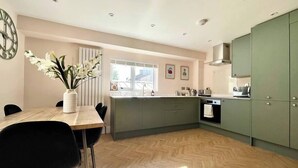 Une cuisine moderne avec une table à manger en bois, des chaises noires, un vase de fleurs, une fenêtre et des meubles de rangement verts.