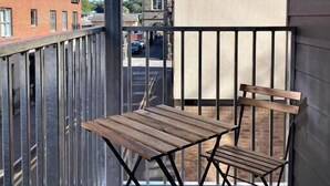Un balcon avec une table et des chaises en bois, une rambarde en métal et une vue sur un immeuble en briques et une rue.