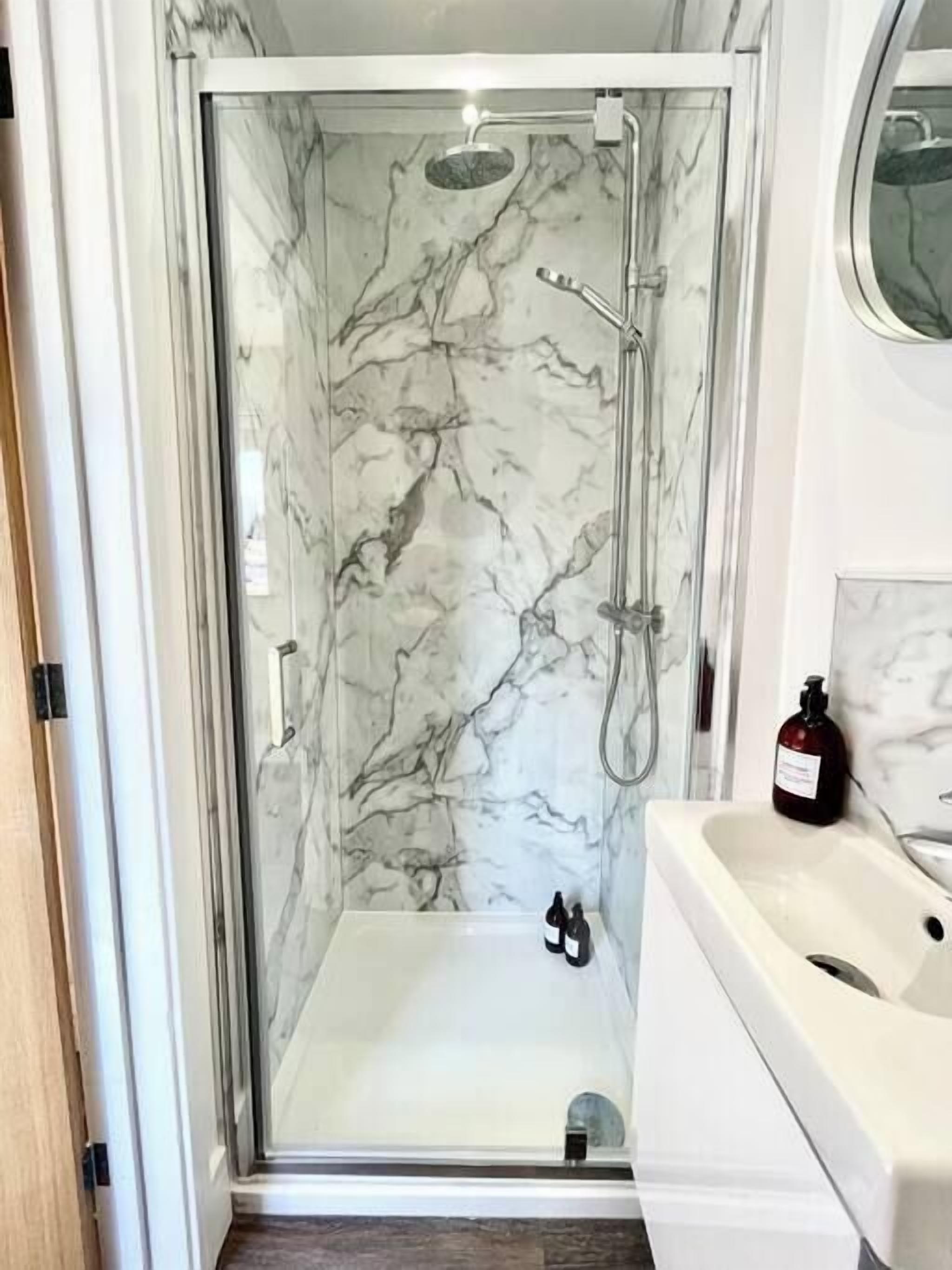 A walk-in shower with marble walls and a white sink.