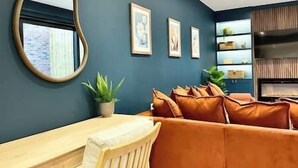 Un salon moderne avec un mur bleu, un miroir rond, une table en bois, des canapés en cuir orange et des tableaux encadrés.