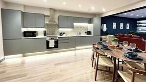 Une cuisine moderne avec des meubles gris, un îlot central et un coin repas comprenant une table et des chaises en bois.