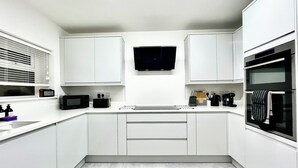 A modern kitchen with white cabinets, a flat-screen TV mounted above the countertop, a microwave, a coffee maker, and an oven. - New and Spacious Apartment - Sleeps 5 (Bristol)