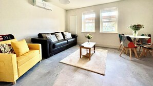 A living room with a black leather sofa, a yellow armchair, a coffee table, and a dining area with a table and chairs. - New and Spacious Apartment - Sleeps 5 (Bristol)