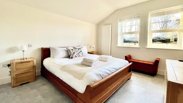 A bedroom with a wooden bed, bedside tables, a bench, and two windows. - New and Spacious Apartment - Sleeps 5 (Bristol)