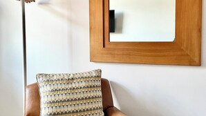 A brown leather armchair with a patterned cushion, a wooden-framed mirror on the wall, and a floor lamp with a white shade. - New and Spacious Apartment - Sleeps 5 (Bristol)