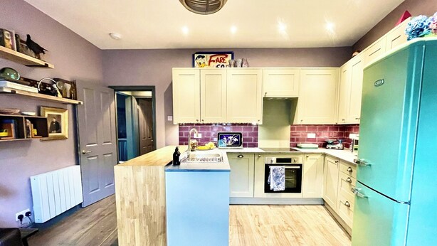 A modern kitchen with light-colored cabinets, a central island, and a built-in oven.