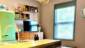 A kitchen with a green refrigerator, wooden cabinets, a bar area with stools, a television, and a window with blinds.