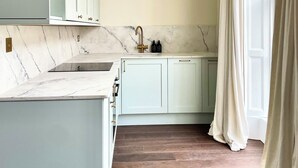 A kitchen with marble countertops, light-colored cabinets, and a wooden floor. - New King Street Suites - Apartment 1 (Bath)