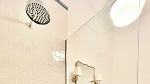 A bathroom with a white tiled wall, a green-tiled shower area, a mirror with wall-mounted lights, and a toilet. - New King Street Suites - Apartment 1 (Bath)