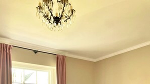 A bedroom with a large bed, a chandelier, a window with curtains, and a radiator.