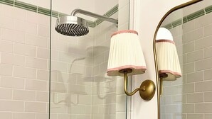 A shower with a glass door, a handheld showerhead, and a wall-mounted light fixture with a pink shade.