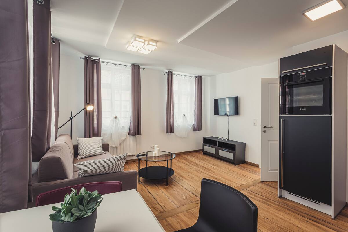 A modern living room with a sofa, a dining table, a coffee table, and a black refrigerator.