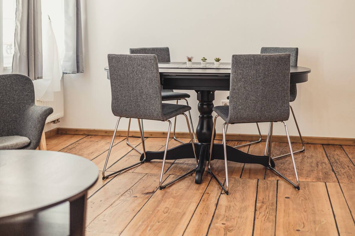 A dining area with a round table, four grey chairs, and a black table base. There are three pendant lights above the table.