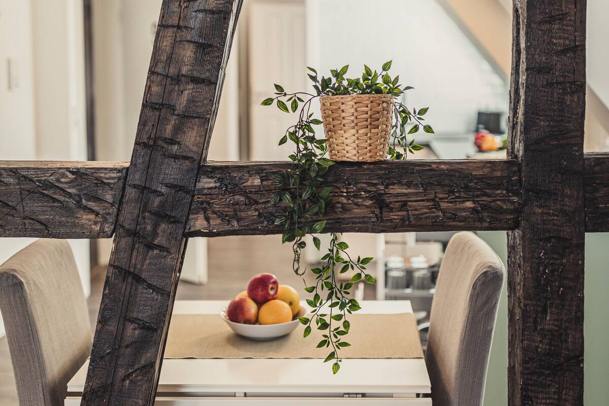 A dining area with a rustic wooden table, a bowl of fruit, and a woven basket with greenery.