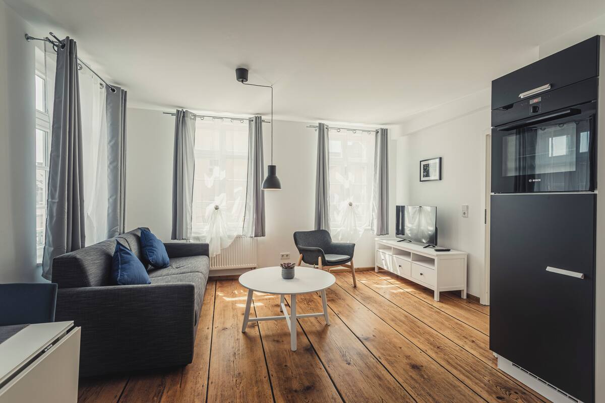 A modern living room with a sofa, a dining table, a chair, a TV, and a black refrigerator.