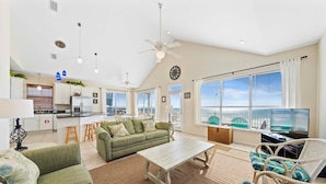 A spacious living area with a green sofa, a white coffee table, wicker chairs, and a view of the city through large windows. - Far Reach II (Gulf Shores)